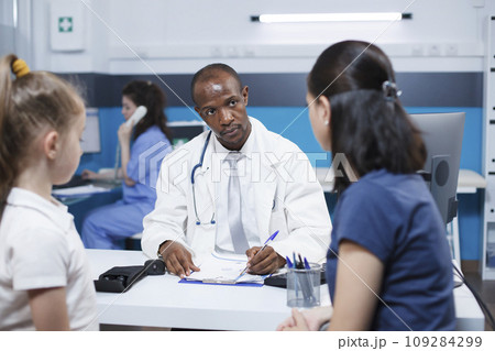 In hospital office, doctor consults with a caucasian woman and her daughter, discussing a medical condition, and providing advice and treatment options. Professional and caring atmosphere. In hospital office, doctor consults with a caucasian woman and her daughter, discussing a medical condition, and providing advice and treatment options. Professional and caring atmosphere. 109284299