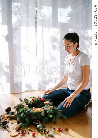 Designer examines the Christmas wreath lying on the floor surrounded by accessories Designer examines the Christmas wreath lying on the floor surrounded by accessories 109284656