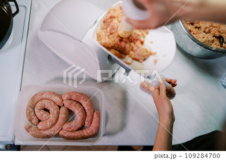 Cook stuffs the gut with minced meat on an electric meat grinder, pushing it with a pusher. Top view Cook stuffs the gut with minced meat on an electric meat grinder, pushing it with a pusher. Top view 109284700