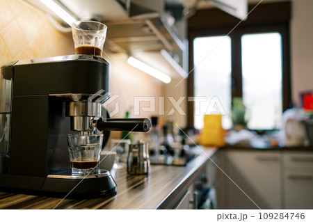 Black coffee dripping from a carob coffee maker into a glass on a stand Black coffee dripping from a carob coffee maker into a glass on a stand 109284746