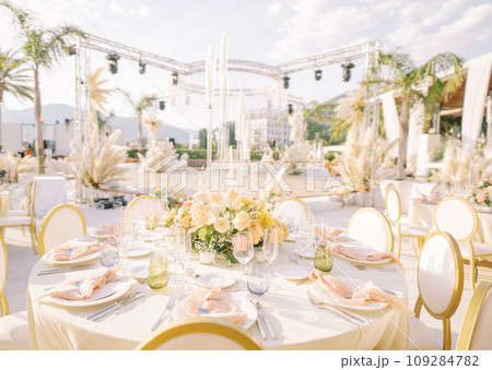 Covered festive tables with bouquets of flowers and candles stand on the open air terrace Covered festive tables with bouquets of flowers and candles stand on the open air terrace 109284782