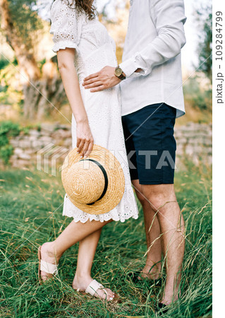 Man hugs woman by the waist standing with a straw hat in her hand in the garden. Cropped. Faceless 109284799