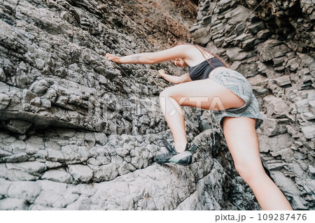 Sports Woman Climbing The Rock. Young woman With slim fit body climbing in volcanic basalt cave with beautiful sea view. The athlete girl trains in nature. Woman overcomes difficult climbing route. Sports Woman Climbing The Rock. Young woman With slim fit body climbing in volcanic basalt cave with beautiful sea view. The athlete girl trains in nature. Woman overcomes difficult climbing route. 109287476