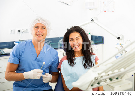 Portrait of a smiling man dentist with a positive woman patient sitting in a dental chair Portrait of a smiling man dentist with a positive woman patient sitting in a dental chair 109289440