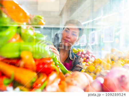 Woman setting out peppers on showcase in greengrocery Woman setting out peppers on showcase in greengrocery 109289524