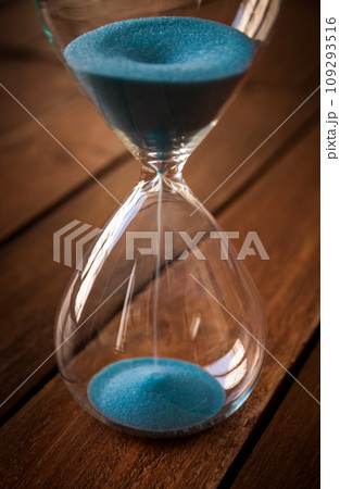 Hourglass containing blue sand on a rustic wooden board 109293516