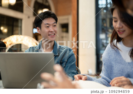 A cheerful young Asian man is listening to his friend's ideas while sitting at a cafe together. 109294859