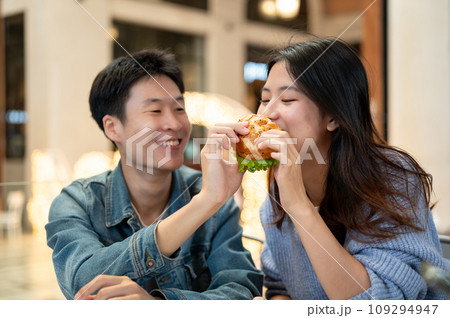 Cheerful young Asian couple enjoys eating a yummy burger on a weekend date at a restaurant. Cheerful young Asian couple enjoys eating a yummy burger on a weekend date at a restaurant. 109294947