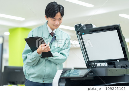オフィスでコピー機をメンテナンスする若い男性の作業員 109295103
