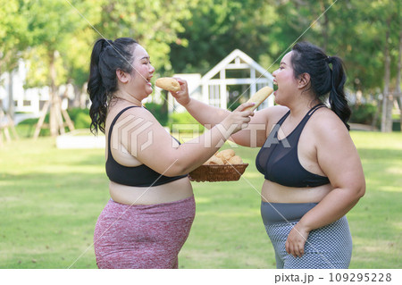 Cheerful two woman overweight in sportswear have fun and enjoy eating bread while exercising Cheerful two woman overweight in sportswear have fun and enjoy eating bread while exercising 109295228