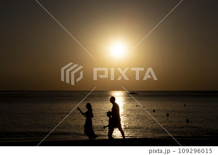 The black silhouette of a happy family against the background of the sun. Father, mother and son are walking along the ocean shore. Lifestyle travel, parents The black silhouette of a happy family against the background of the sun. Father, mother and son are walking along the ocean shore. Lifestyle travel, parents 109296015