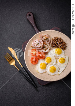 Delicious nutritious breakfast of fried quail eggs, bacon, legumes and cherry tomatoes 109297931