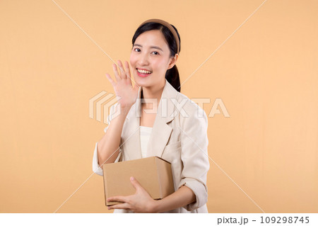 portrait of happy successful confident young asian business woman wearing white jacket holding parcel box isolated on beige studio background, Delivery courier and shipping service concept. portrait of happy successful confident young asian business woman wearing white jacket holding parcel box isolated on beige studio background, Delivery courier and shipping service concept. 109298745