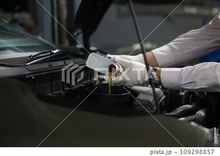 Auto mechanic pours oil into car engine from cans of oil Auto mechanic pours oil into car engine from cans of oil 109298857