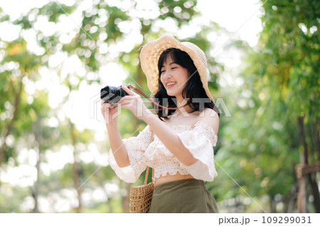 Portrait of asian young woman traveler with weaving hat and basket and a camera on green public park nature background. Journey trip lifestyle, world travel explorer or Asia summer tourism concept. 109299031