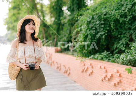 Portrait of asian young woman traveler with weaving hat and basket and a camera on green public park nature background. Journey trip lifestyle, world travel explorer or Asia summer tourism concept. Portrait of asian young woman traveler with weaving hat and basket and a camera on green public park nature background. Journey trip lifestyle, world travel explorer or Asia summer tourism concept. 109299038