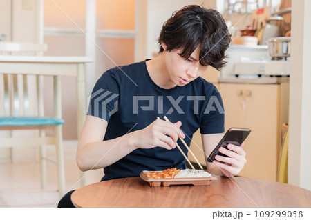 家でコンビニ弁当を食べる若い男性 109299058