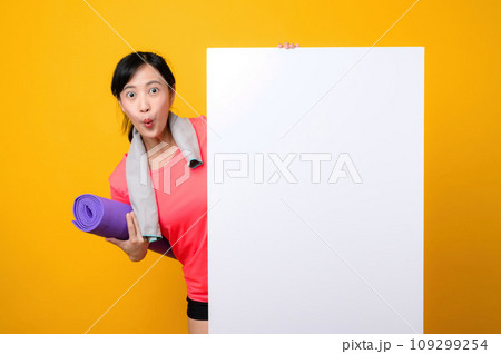 young asian sports fitness woman happy smile wearing pink sportswear standing behind the white blank banner or empty space advertisement board against yellow background. wellbeing lifestyle concept. young asian sports fitness woman happy smile wearing pink sportswear standing behind the white blank banner or empty space advertisement board against yellow background. wellbeing lifestyle concept. 109299254