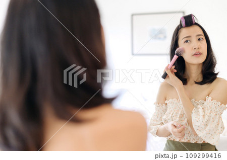 Beautiful young Asian woman applying makeup in front of the mirror. Lifestyle people concept. Advertisement for skin cream, anti-wrinkle cream, baby face 109299416
