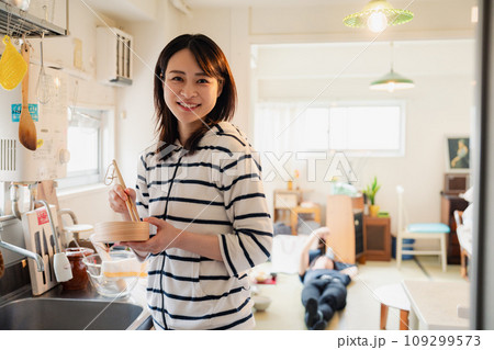 妻がお弁当を作っている後ろで寝転ぶ夫 妻がお弁当を作っている後ろで寝転ぶ夫 109299573