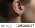 Pierce the ear with an earring. Closeup of female ear with three earrings. 109300027