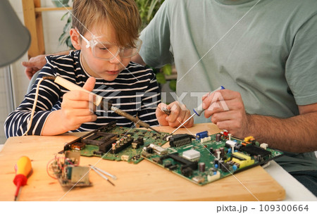 Father with his son spend time together. Close-up of a man teaching his boy at home to solder computer spare parts. Education moment during parenthood. Togetherness concept. 109300664