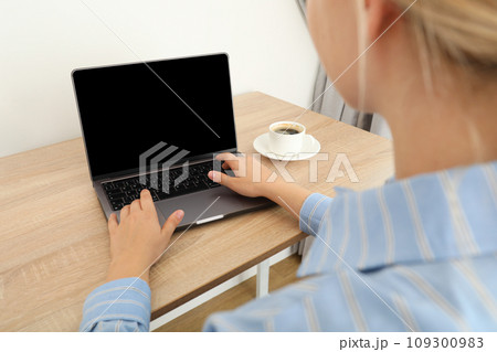 A woman with a cup of coffee is working on a laptop A woman with a cup of coffee is working on a laptop 109300983