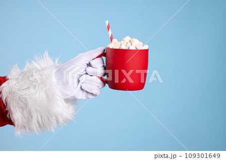 Cup with marshmallows in Santa's hand on blue background 109301649
