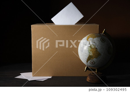 Voting box and globe on wooden table on black background Voting box and globe on wooden table on black background 109302495
