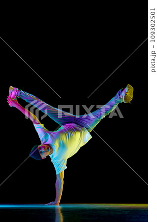 Hand stand. Swipe. Young flexible athletic man dancing breakdance freezes in sport outfit against black background in neon light. 109302501