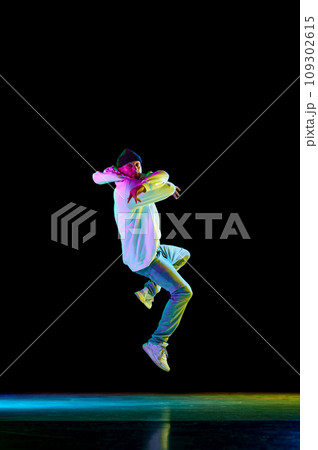 Modern dance. Breakdance male dancer, athletic guy dancing freestyle in stylish outfit against black background in neon light. 109302615