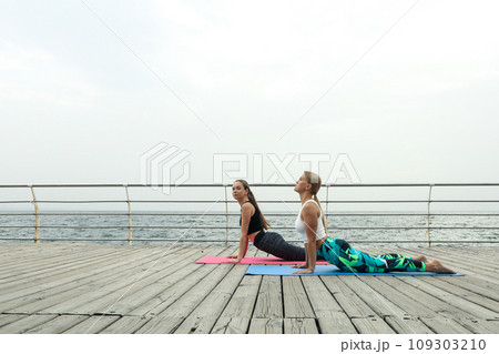 Two young women on yoga mats on wooden floor outdoors, space for text Two young women on yoga mats on wooden floor outdoors, space for text 109303210