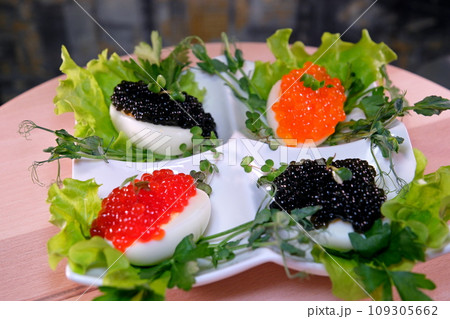 Put black caviar on an egg to serve delicious healthy food Halves of a hard-boiled chicken egg with red caviar on a wooden background. Put black caviar on an egg to serve delicious healthy food Halves of a hard-boiled chicken egg with red caviar on a wooden background. 109305662