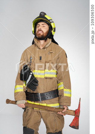 Exhausted caucasian firefighter with closed eyes, holding shabby axe. Front view of tired, bearded man in uniform with hatchet resting, on gray studio background. Concept of job, workplace, equipment. Exhausted caucasian firefighter with closed eyes, holding shabby axe. Front view of tired, bearded man in uniform with hatchet resting, on gray studio background. Concept of job, workplace, equipment. 109306500