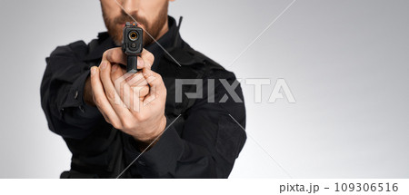Looking down barrel of anonymous police officer's sidearm in studio. Crop view of unrecognizable constable aiming, by pointing handgun to camera, isolated on gray. Concept of danger, work, weapon. 109306516
