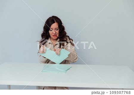 Beautiful brunette woman tearing paper at table negative emotions Beautiful brunette woman tearing paper at table negative emotions 109307768