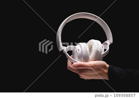 Wireless headphones on a black background. White full-size noise-canceling headset with built-in microphone. Side view of acoustic stereo sound system in female hand 109308857