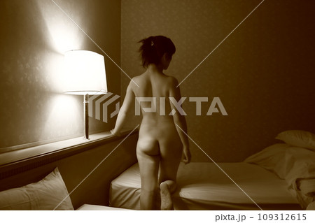 女性ヌード後ろ姿背中立ちポーズ、暗いライティングに浮かぶ体のシルエット 109312615