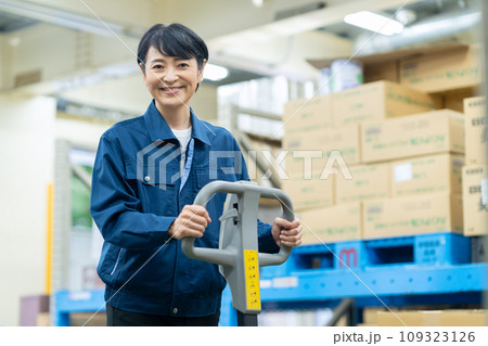 倉庫でハンドリフトを使って荷物を運ぶミドルの女性作業員 109323126