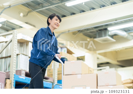 倉庫でハンドリフトを使って荷物を運ぶミドルの女性作業員 倉庫でハンドリフトを使って荷物を運ぶミドルの女性作業員 109323131