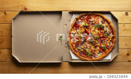 Pepperoni pizza with bell peppers sweetcorn and arugula in open carton box on natural wooden kitchen table flat lay view with copy-space Pepperoni pizza with bell peppers sweetcorn and arugula in open carton box on natural wooden kitchen table flat lay view with copy-space 109323844