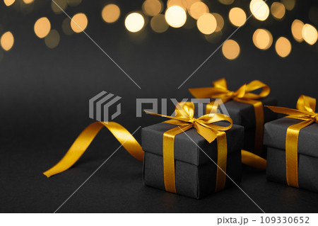 Black gift box with golden ribbon bow on black background Black gift box with golden ribbon bow on black background 109330652