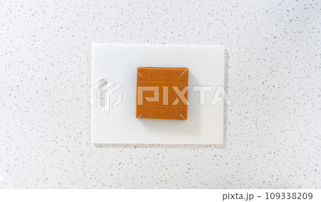 Flat lay. Cutting caramel fudge into square pieces on a white cutting board. 109338209
