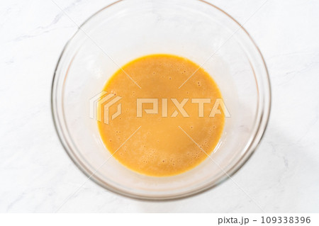 Mixing ingredients with a hand mixer in a small mixing bowl to make the eggnog caramel sauce. 109338396