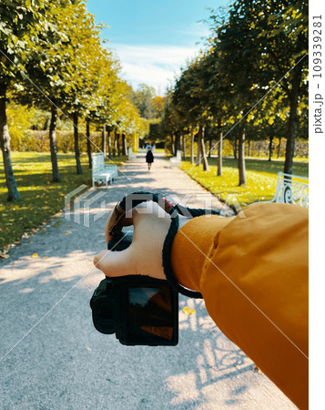 In a park, amidst trees, a man photographs a girl walking on a path, showcasing a first-person viewpoint. pov 109339281