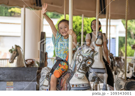 メリーゴーランドに乗ってはしゃぐ女の子と母親 109343001
