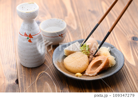 小皿に取り分けたおでんと日本酒の熱燗 山椒の葉を添えて 小皿に取り分けたおでんと日本酒の熱燗 山椒の葉を添えて 109347279