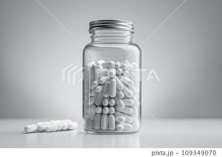 Transparent supplement bottle filled with white capsules against a gray smooth backdrop Transparent supplement bottle filled with white capsules against a gray smooth backdrop 109349070