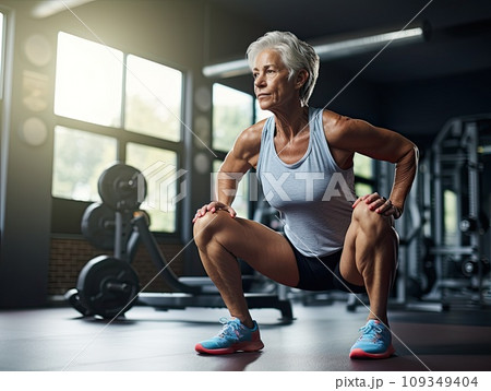 Senior gray elderly woman doing squats workout in a gym. 109349404