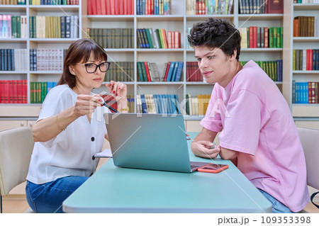 Woman mentor teaching male student in college library, exam preparation Woman mentor teaching male student in college library, exam preparation 109353398